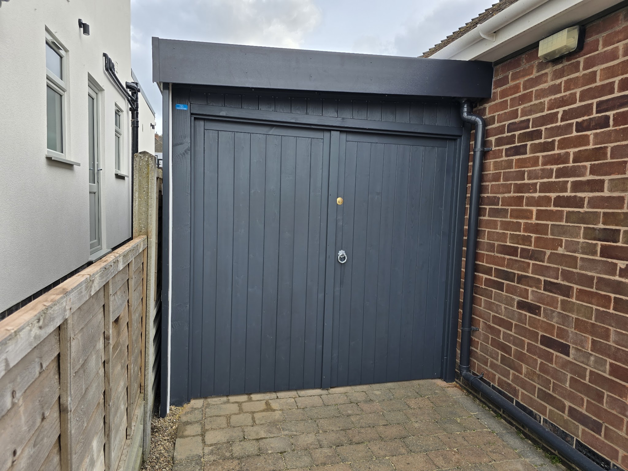 Grey painted pair of solid timber gates between two buildings on a block-paved path