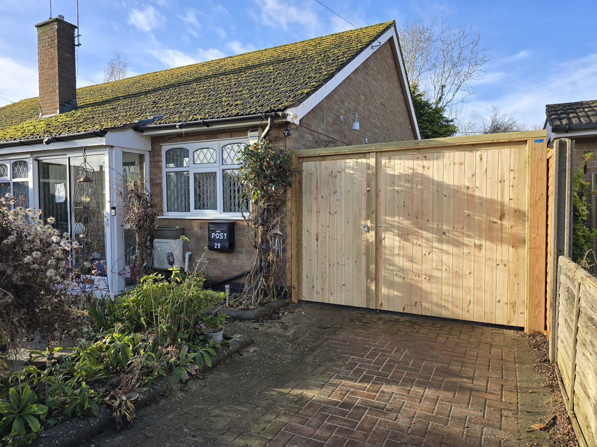 Natural timber double driveway gates beside a bungalow on a block-paved drive