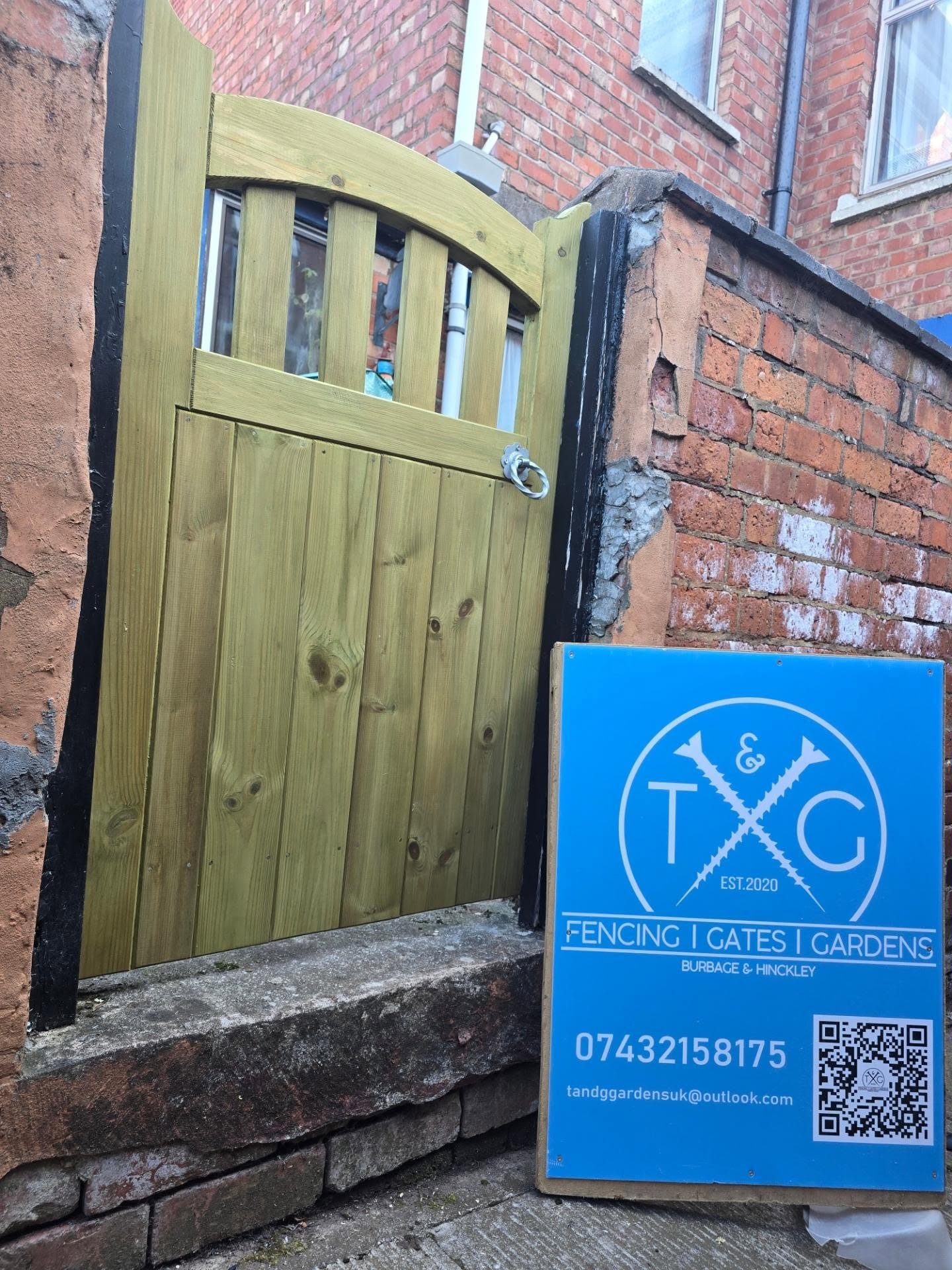 Timber side gate with a slatted, curved top section in a brick opening, with the T&G sign board