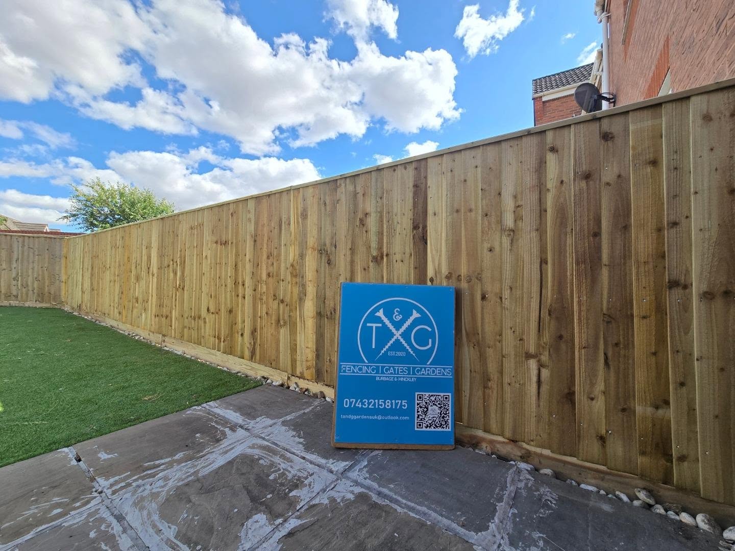 Long run of new closeboard fencing around a garden with artificial grass, with the T&G sign board